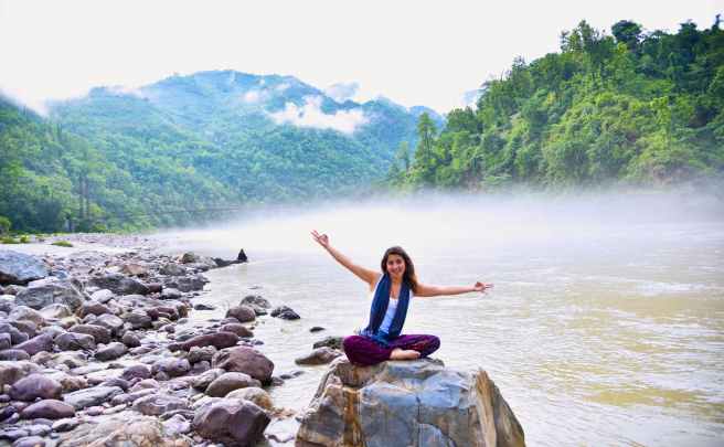 photo of woman sitting on stone next to body of water